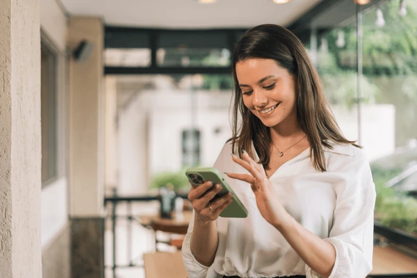 A young woman smiling while using her phone indoors.
