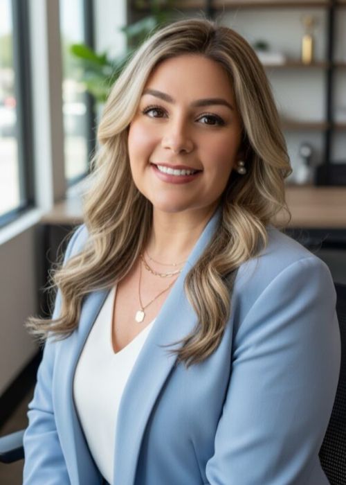 Professional woman in a light blue blazer smiling indoors.