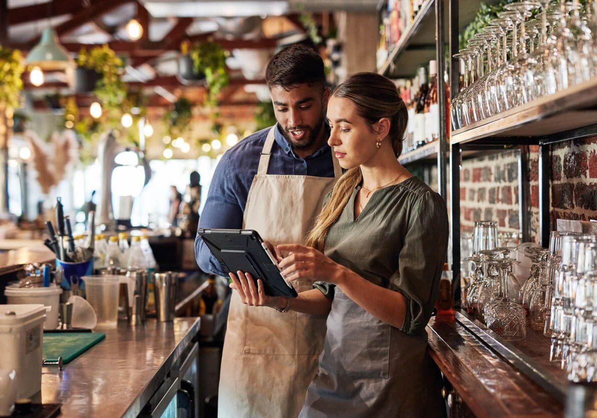 Two baristas checking orders on a tablet behind the counter.