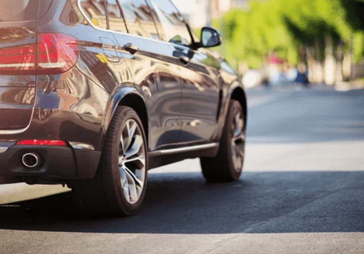 Close-up of a car's rear wheel and side on a sunny day.