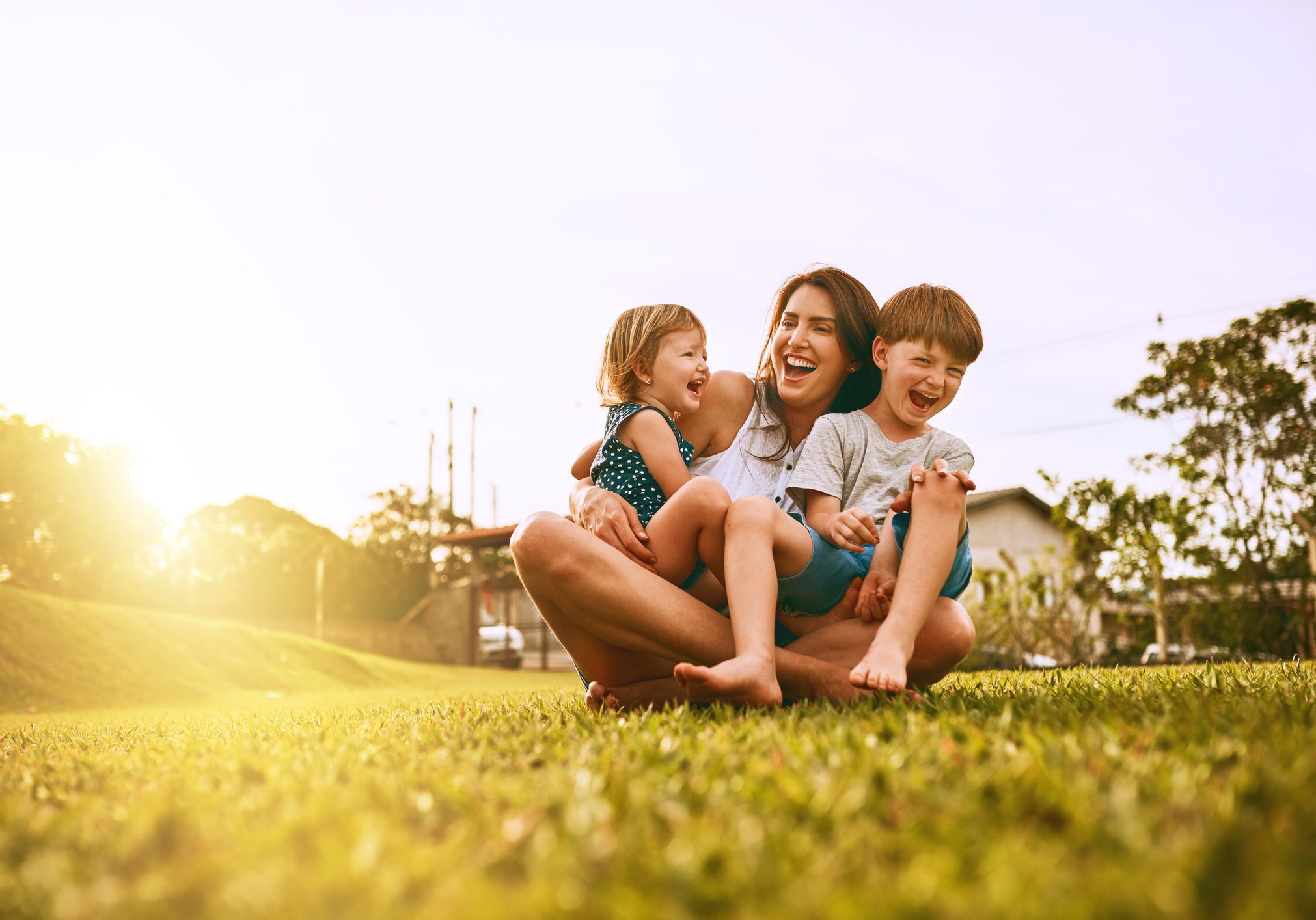 Happy children playing and laughing outdoors on grass at sunset.