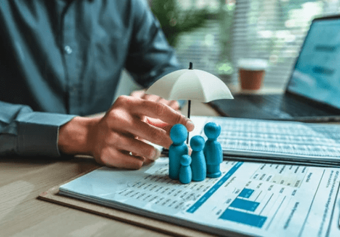 Hand protecting small blue figures under an umbrella on financial documents.